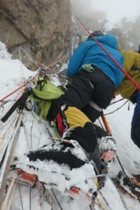 an equiped climber is climbing up a rocky snowy mountain.