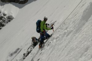 two people climbing up a snow covered mountain.