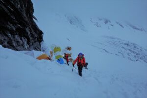 a group of people walking up a snowy mountain with tents.