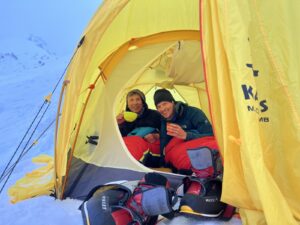 two people sitting inside a yellow tent in the snow.
